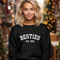 Woman wearing black Varsity Besties Crewneck Sweatshirt with white varsity-style lettering Besties EST. 2025 in festive indoor setting