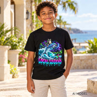 Boy wearing a black Local Legend kids graphic T-shirt with a cat riding a dolphin through neon waves in a sunlit coastal courtyard.
