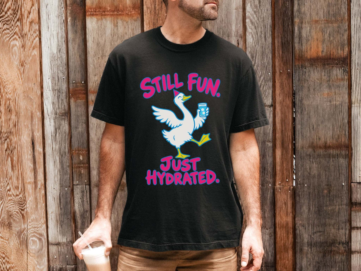 Male model wearing black Comfort Colors crewneck t-shirt featuring a graphic of a white goose holding a blue water bottle, with the pink text 'STILL FUN. JUST HYDRATED.