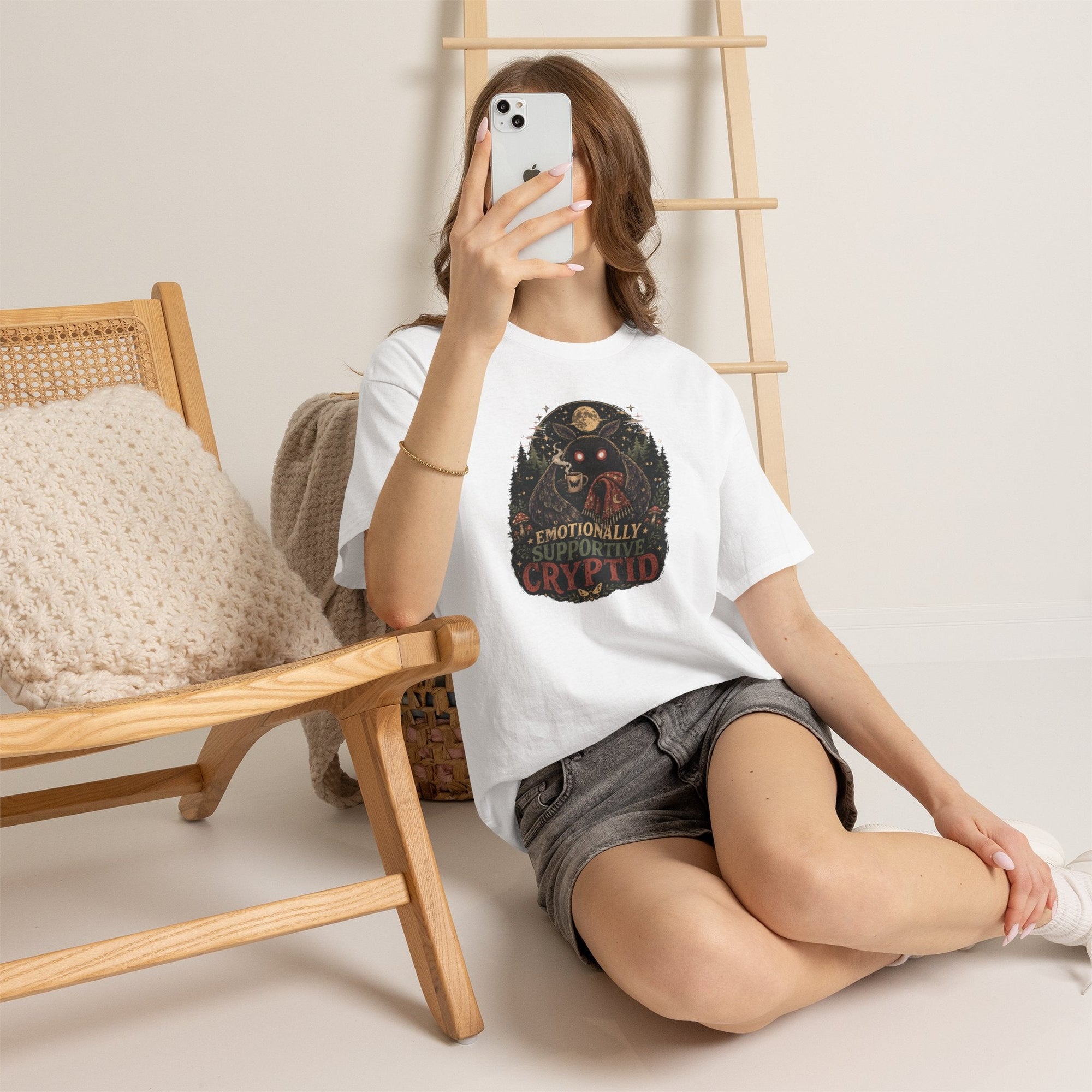 Surreal Mothman cryptid tee with glowing eyes wrapped in blanket holding coffee under moonlit forest canopy