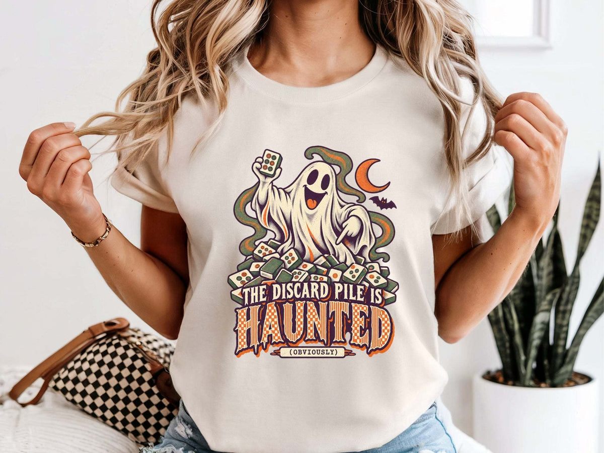 Model wearing ivory Comfort Colors 1717 Halloween mahjong T-shirt with a ghost holding a tile and “The Discard Pile Is Haunted (Obviously)” lettering.