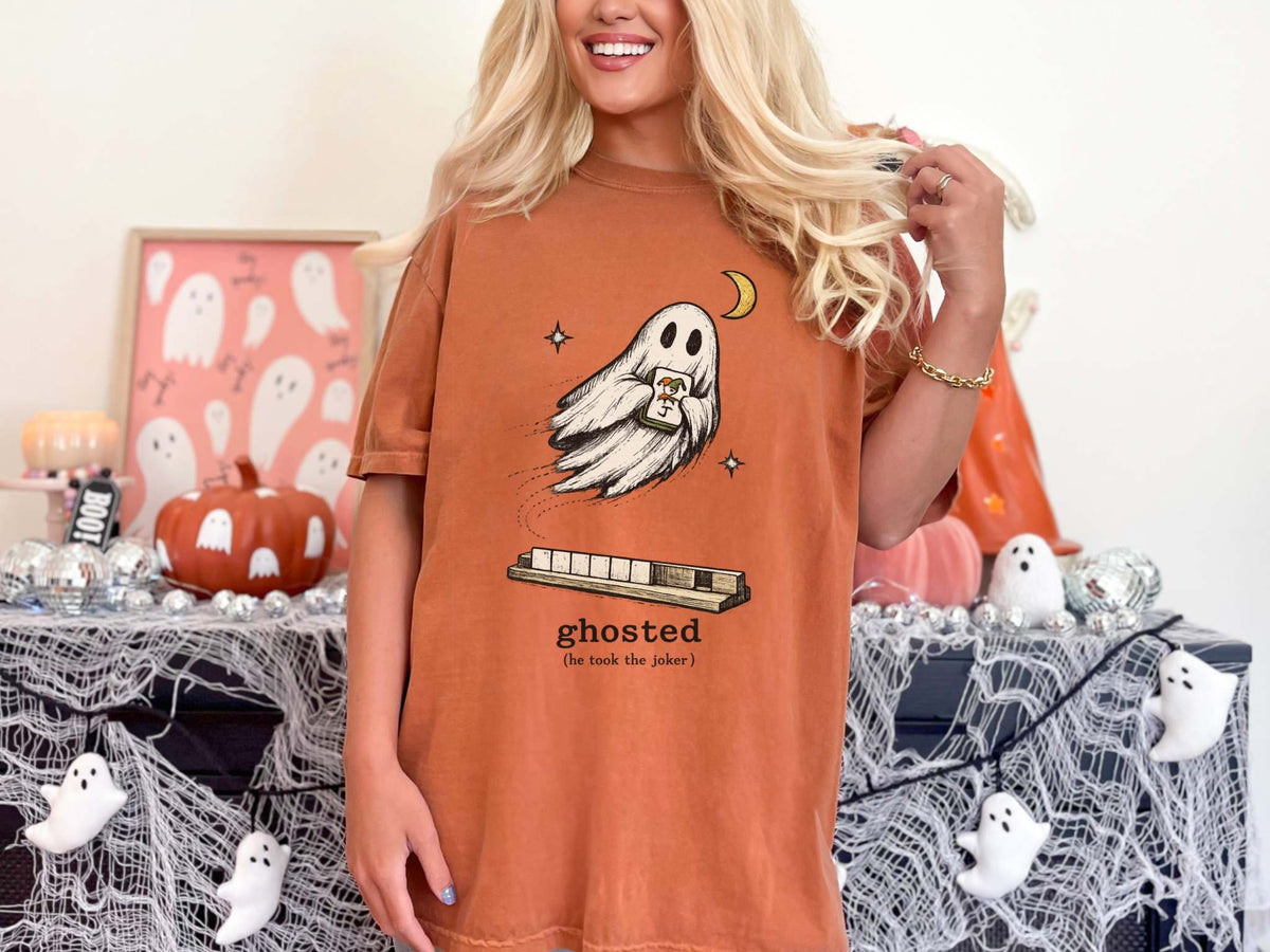 Model wearing a yam orange mahjong T-shirt with a ghost holding a joker tile above a tile rack and “ghosted (he took the joker)” lettering.