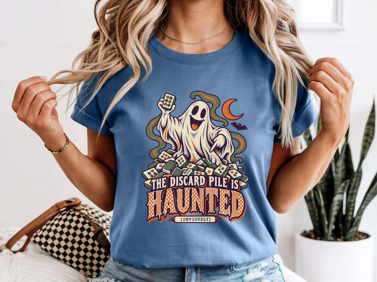 Model wearing blue jean Comfort Colors 1717 Halloween mahjong T-shirt with a ghost holding a tile and “The Discard Pile Is Haunted (Obviously)” lettering.