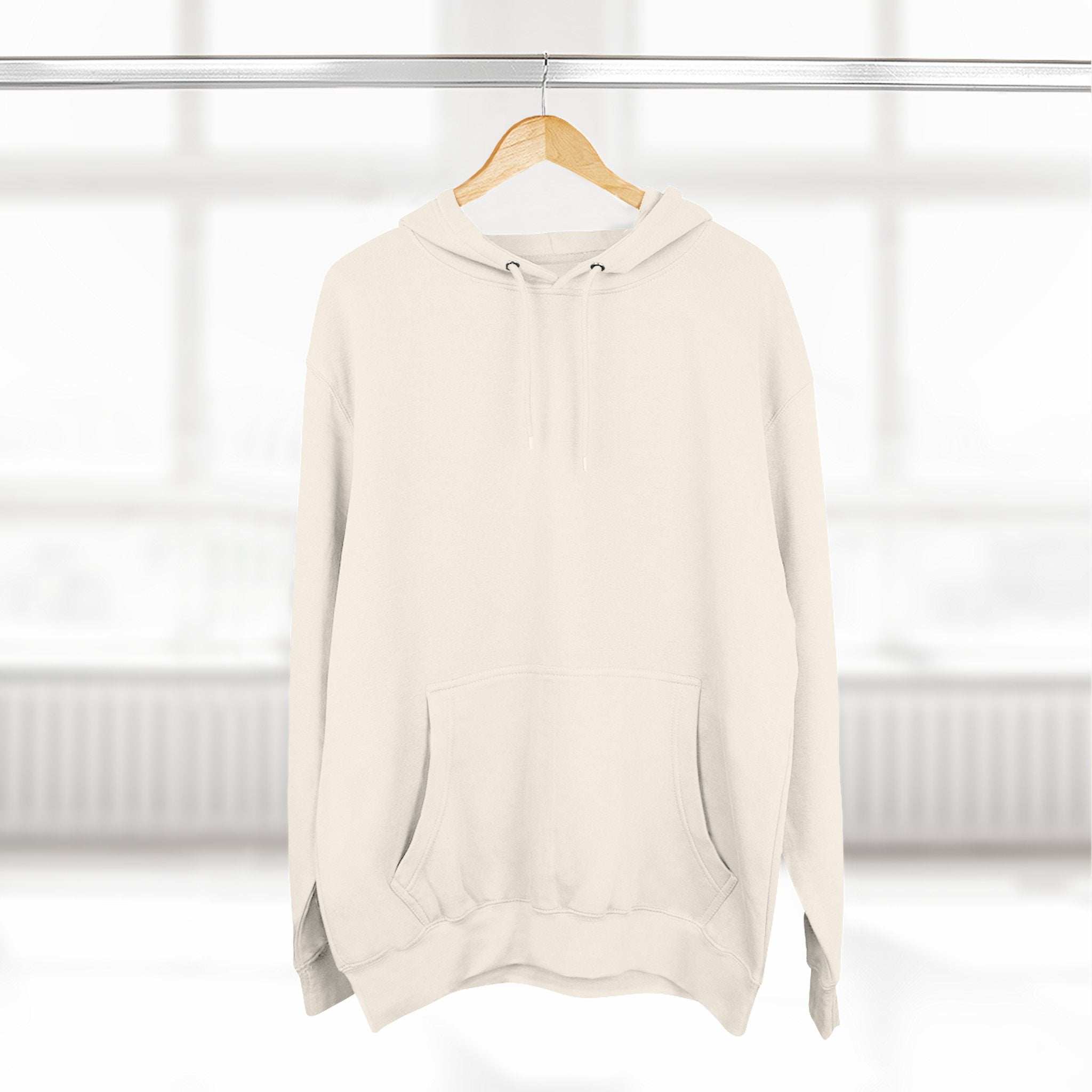 Cream fleece hoodie with adjustable hood and front pocket hanging on wooden hanger in bright room