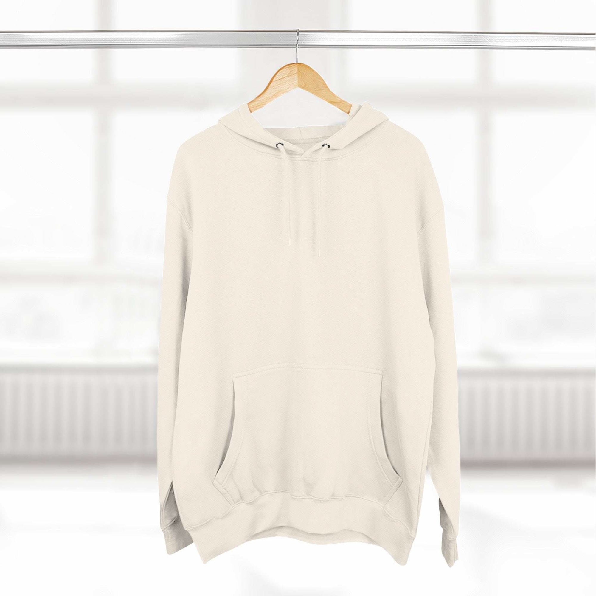 Cream fleece hoodie with adjustable hood and front pocket hanging on wooden hanger in bright room