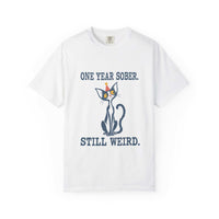 Flat lay of an white Comfort Colors 1717 t-shirt featuring a navy cat in a red party hat and “One Year Sober. Still Weird.” lettering.