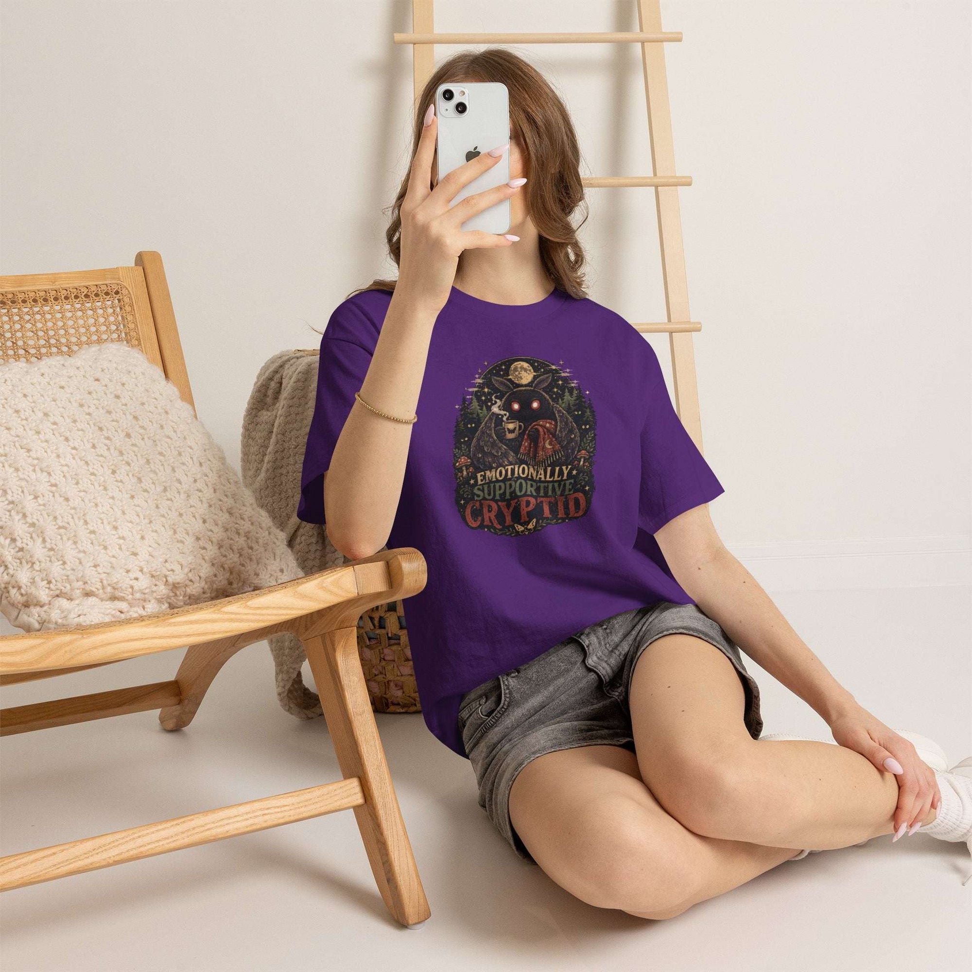 Surreal glowing-eyed mothman cryptid wrapped in blanket holding mug on cryptid tee