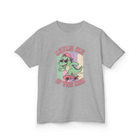 A heather gray short-sleeve t-shirt with a colorful graphic of a cartoon green dinosaur riding a pink skateboard, with the text 'CATCH ME IF YOU CAN' in pink.