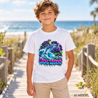 Boy wearing a white Local Legend kids T-shirt with a neon cat riding a dolphin graphic and tan shorts on a sunny beach boardwalk.