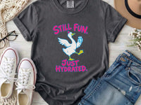 A pepper gray crewneck t-shirt featuring a graphic of a white goose holding a blue water bottle, with the pink text 'STILL FUN. JUST HYDRATED.