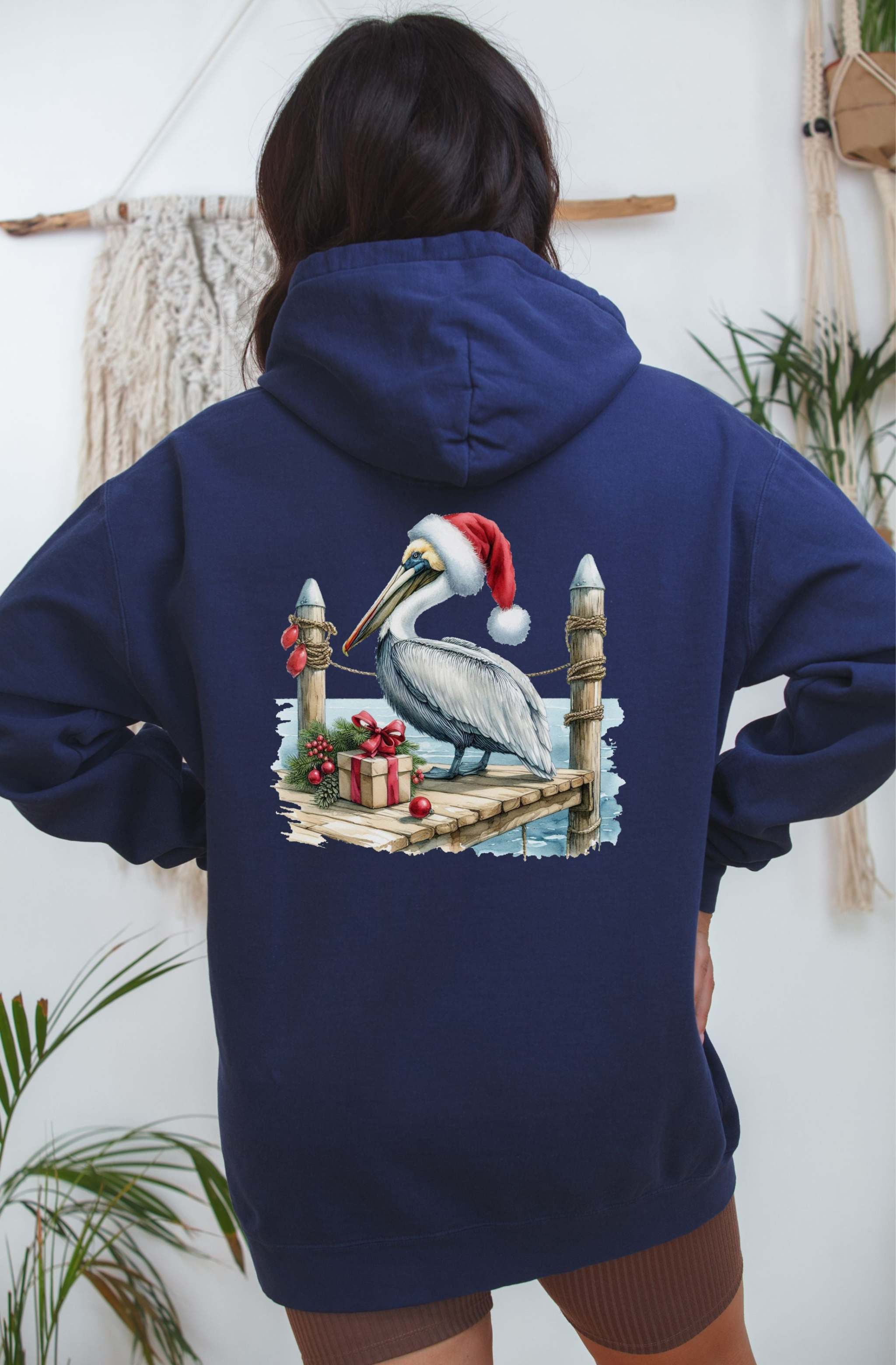 Navy hoodie featuring a pelican in a Santa hat on a dock with holiday decorations