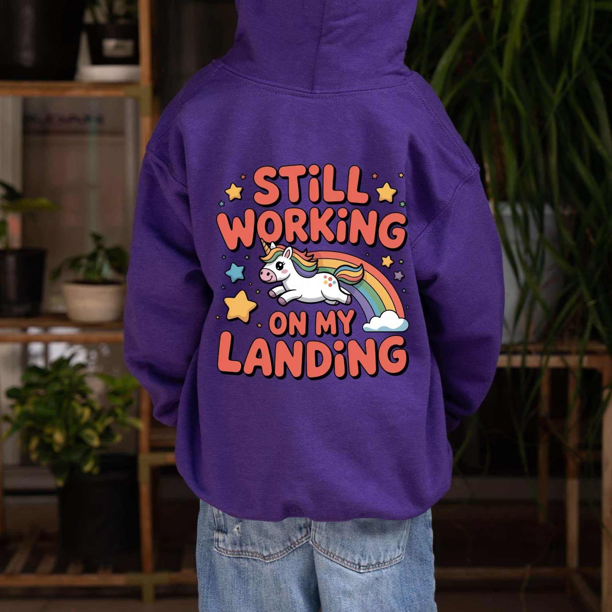 Kids hoodie with colorful unicorn rainbow design and playful "Still Working On My Landing" text