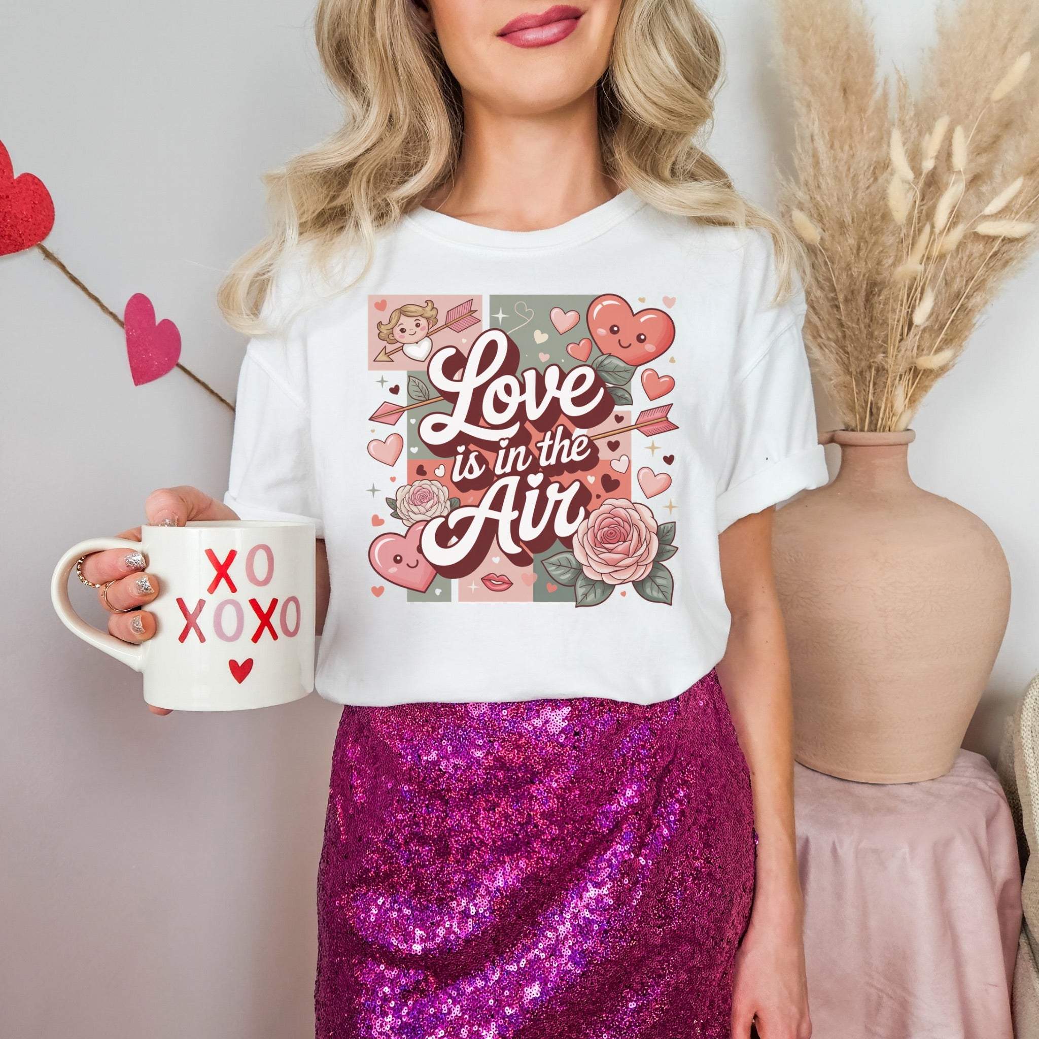 Valentine's Love Is in the Air white t-shirt with hearts and rose design worn by woman holding XOXO mug