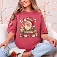 Model wearing a Crimson red Comfort Colors T-shirt with Santa holding a mahjong tile above a tile rack and cream “Cozy But Competitive” lettering.