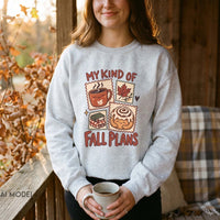 Woman wearing an ash grey My Kind of Fall Plans sweatshirt with cozy autumn graphics, holding a ceramic mug on a wooden porch.