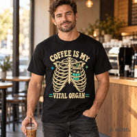 Man holding iced coffee in a café while wearing a black Comfort Colors 1717 skeleton coffee T-shirt reading “Coffee Is My Vital Organ.”