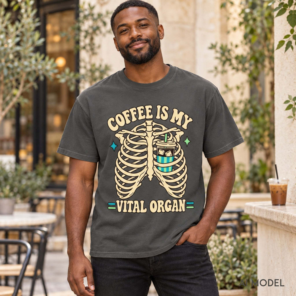 Man modeling a pepper Comfort Colors 1717 “Coffee Is My Vital Organ” T-shirt with a skeleton ribcage graphic in a café courtyard.