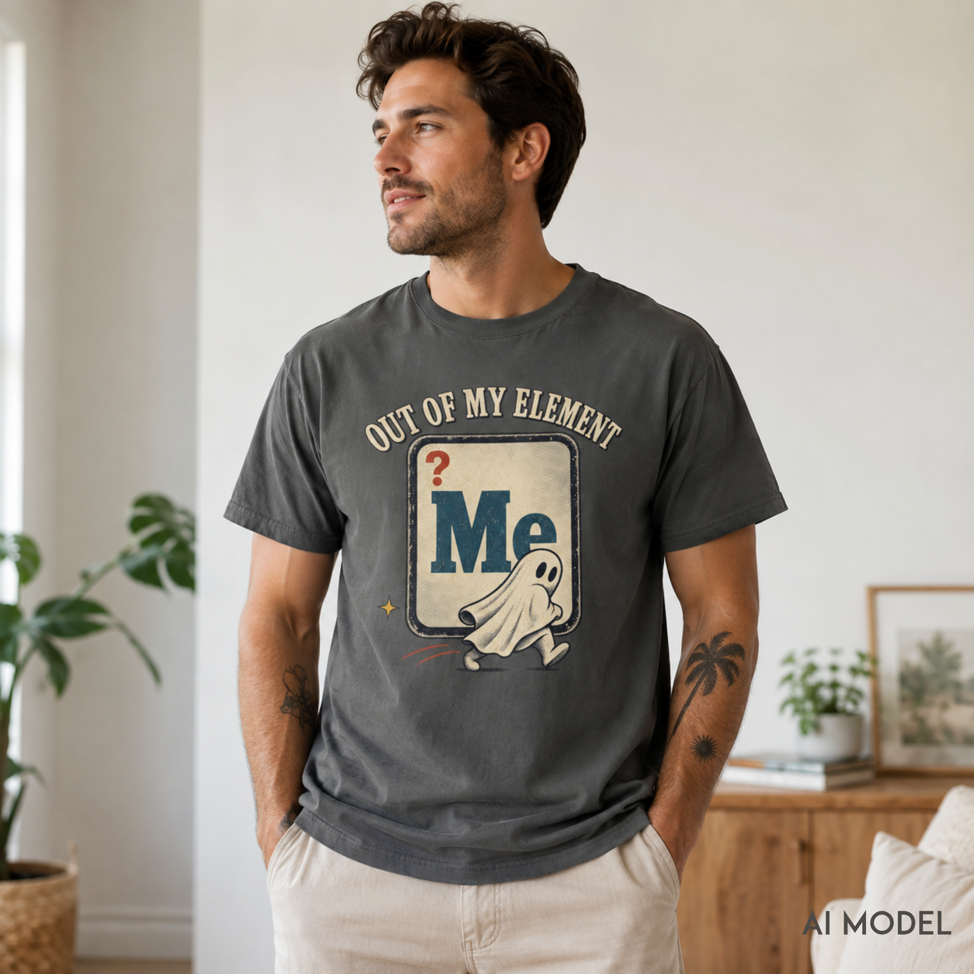 Male model wearing a pepper gray “Out of My Element” ghost graphic T-shirt with a distressed retro design in a softly lit modern interior.