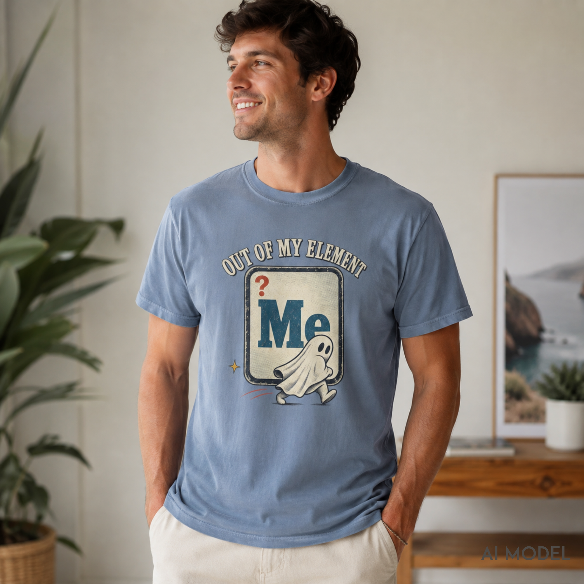 Smiling male model wearing a light blue “Out of My Element” ghost graphic T-shirt with a vintage chemistry-inspired design in a bright home setting.