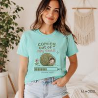     Woman seated in a cozy room wearing a chalky mint “Coming Out of My Shell” snail graphic tee with light-wash jeans.