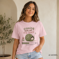     Woman seated in a cozy room wearing a blossom pink “Coming Out of My Shell” snail graphic tee with light-wash jeans.