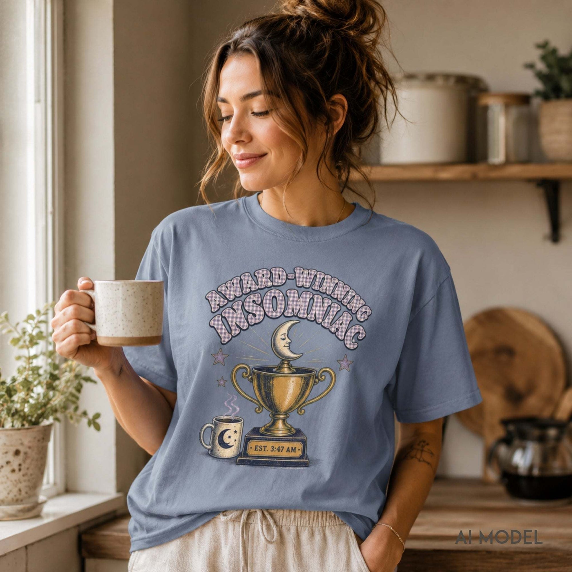     Female model wearing a light blue Award-Winning Insomniac T-shirt with vintage moon, coffee and trophy artwork in a relaxed morning setting.