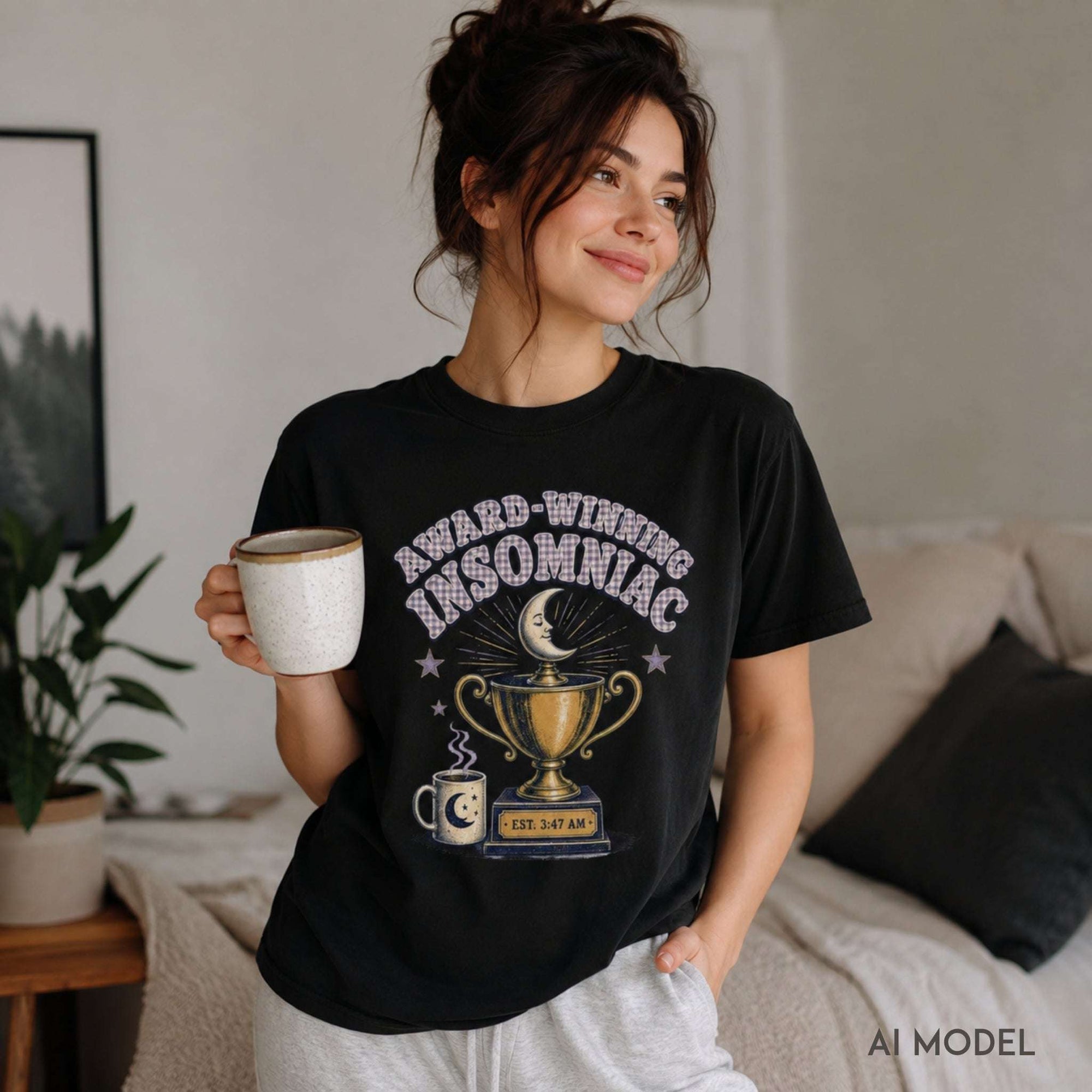 Female model wearing a black Award-Winning Insomniac graphic tee with moon, trophy and coffee cup design while holding a mug at home.