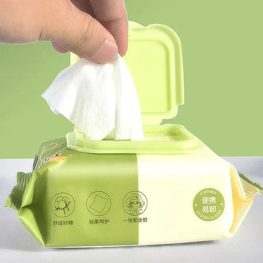 Hand pulling a white wet wipe from a green and cream colored pack of olive plant extract makeup remover wet wipes