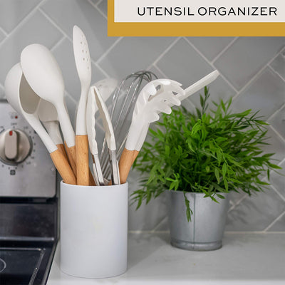 White silicone spatula set with wooden handles in a white utensil organizer on kitchen countertop next to potted green plant