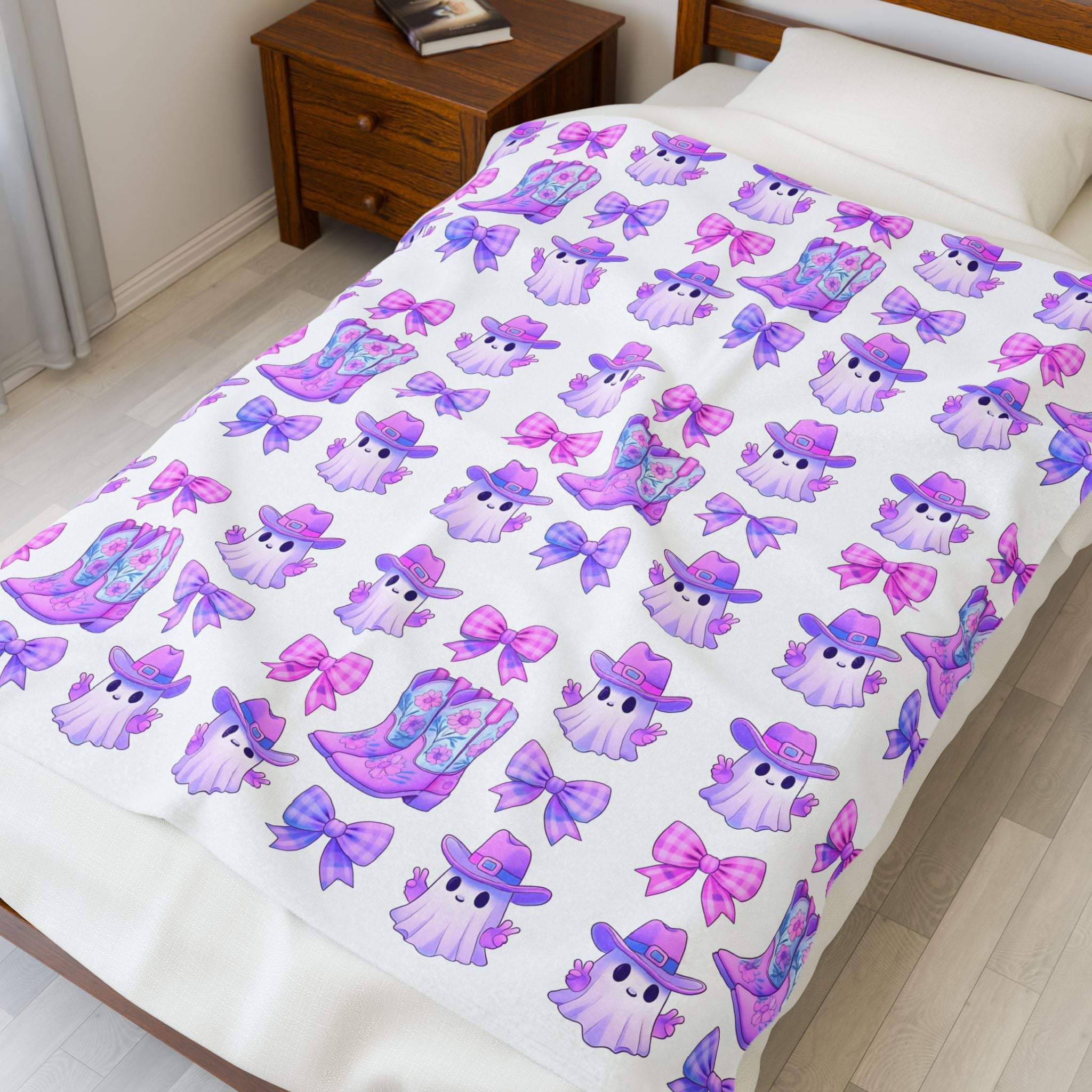 Pink ghost blanket with purple cowboy hats and boots on a white plush throw blanket on bed