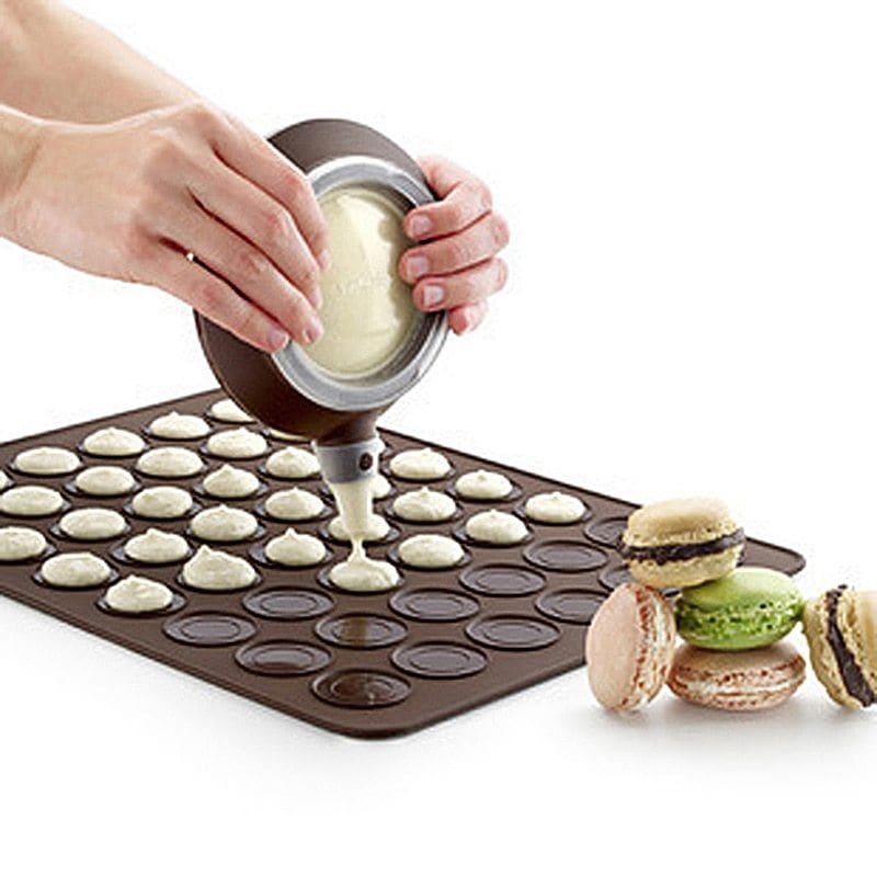 Silicone kitchen bakeware mat with circular molds being filled for baking macarons, showing flexible non-stick surface and finished macarons beside it.