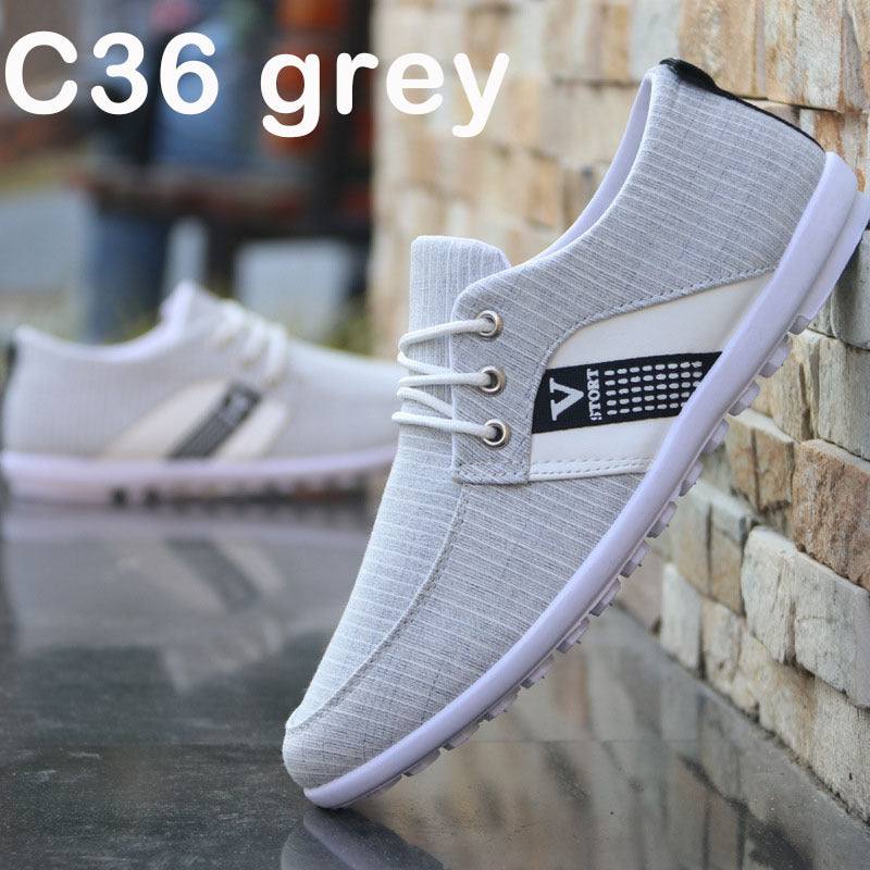 Grey men's soft-soled canvas leisure shoes with round toe and low heel against a brick wall backdrop