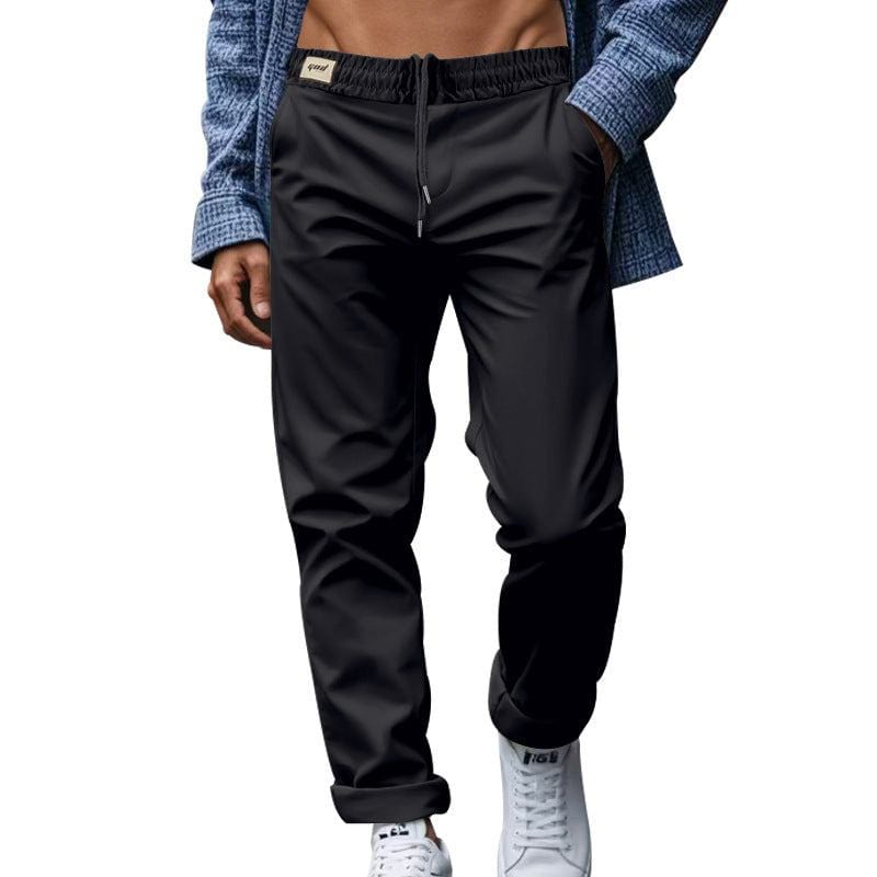 Men's black casual loose fit trousers with pockets and waist tie, styled with a blue jacket and white sneakers.