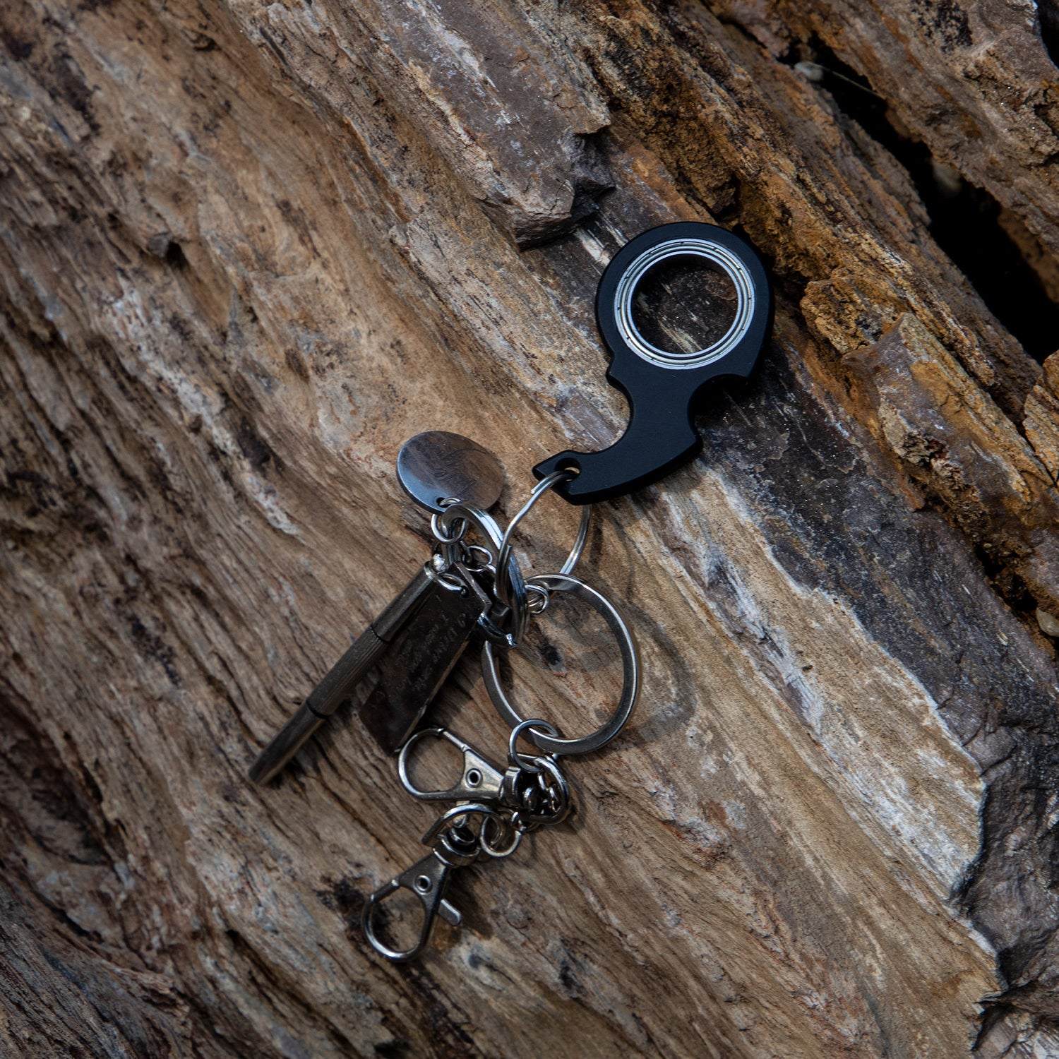Black fidget spinner toy keychain with bottle opener attached to keys on wooden surface