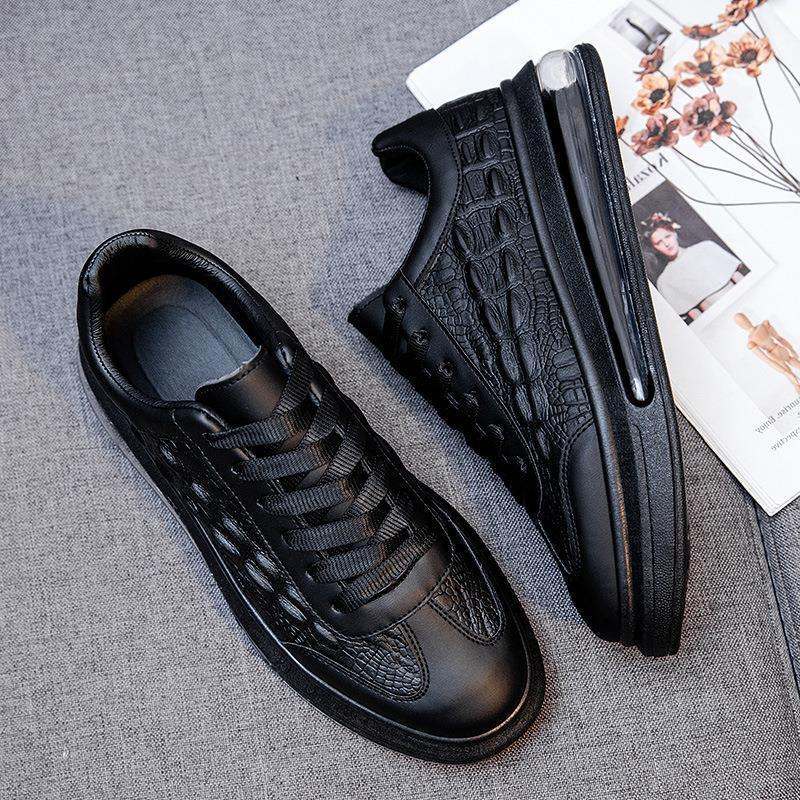 Black trendy leather men's casual sneakers with textured design and rubber sole on gray surface next to magazines.