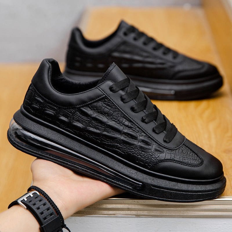 Black trendy leather men's casual sneakers with textured design and rubber sole held in hand on wooden surface