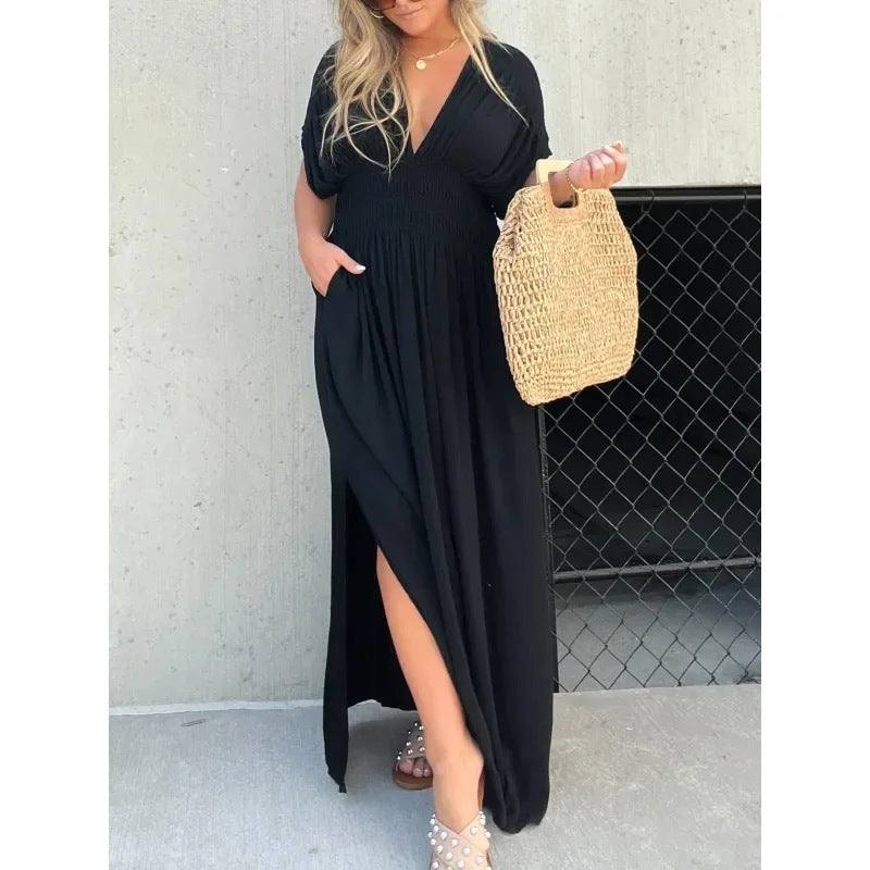 Woman wearing black bat-sleeved V-neck slit long summer dress with elastic waist and holding woven handbag