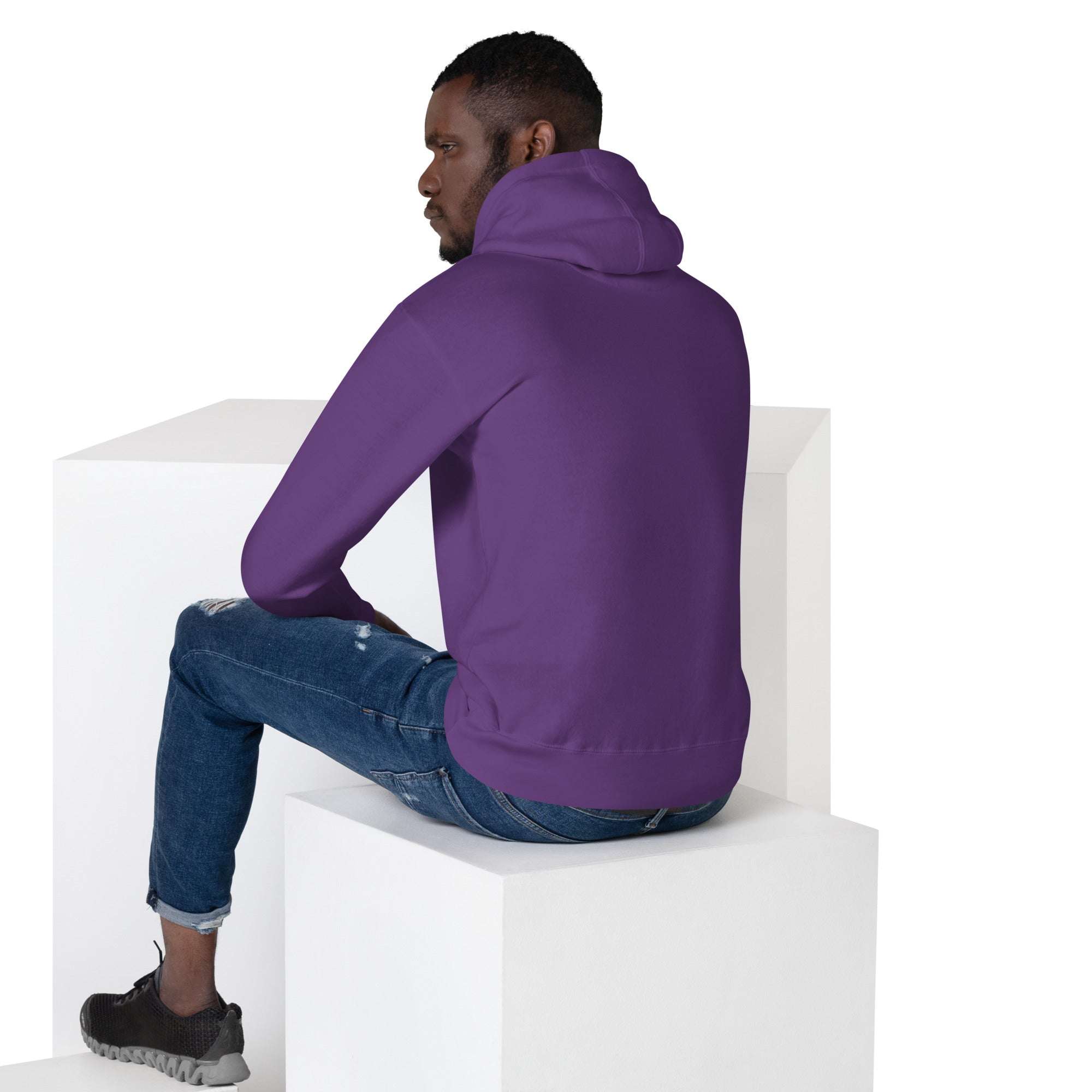 Man wearing purple Basketball Dunk Hoodie sitting on white cubes viewed from back, paired with blue jeans and black sneakers