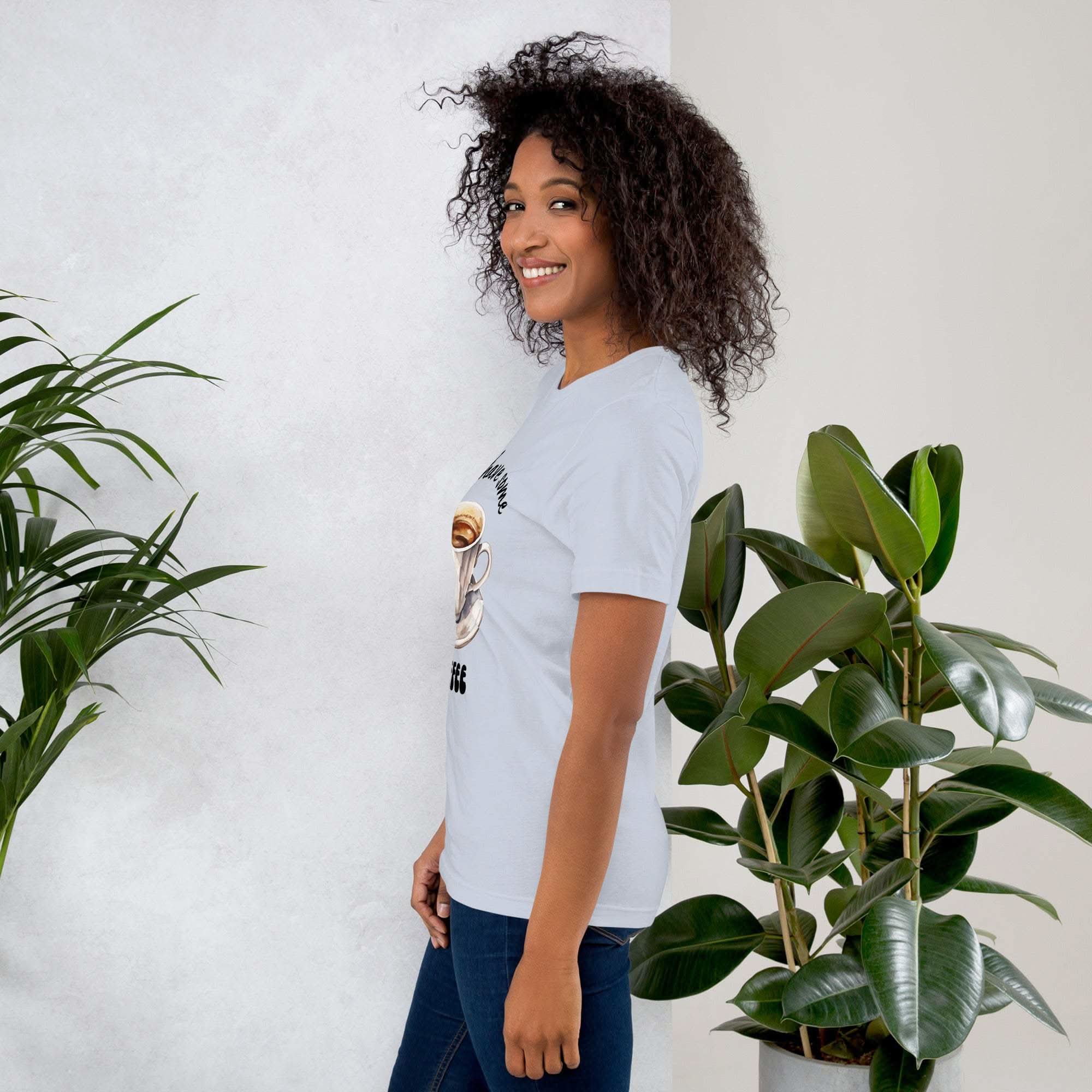 Woman wearing a white coffee t-shirt with coffee-themed design standing next to green plants