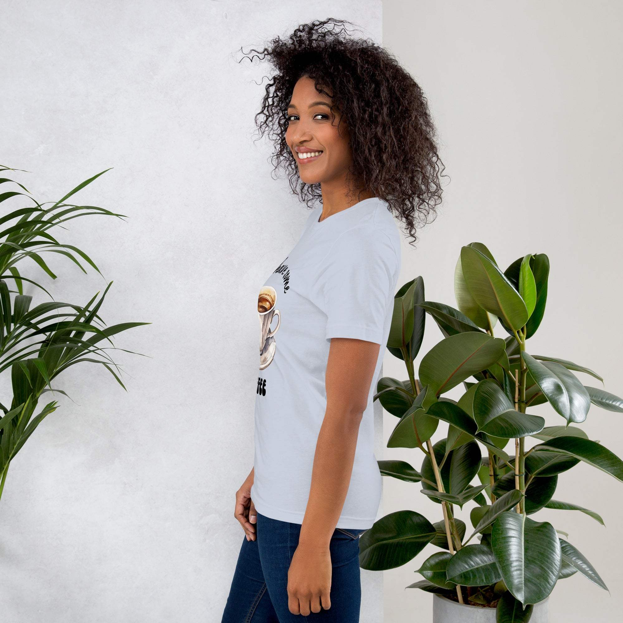 Woman wearing a white coffee t-shirt with coffee-themed design standing next to green plants