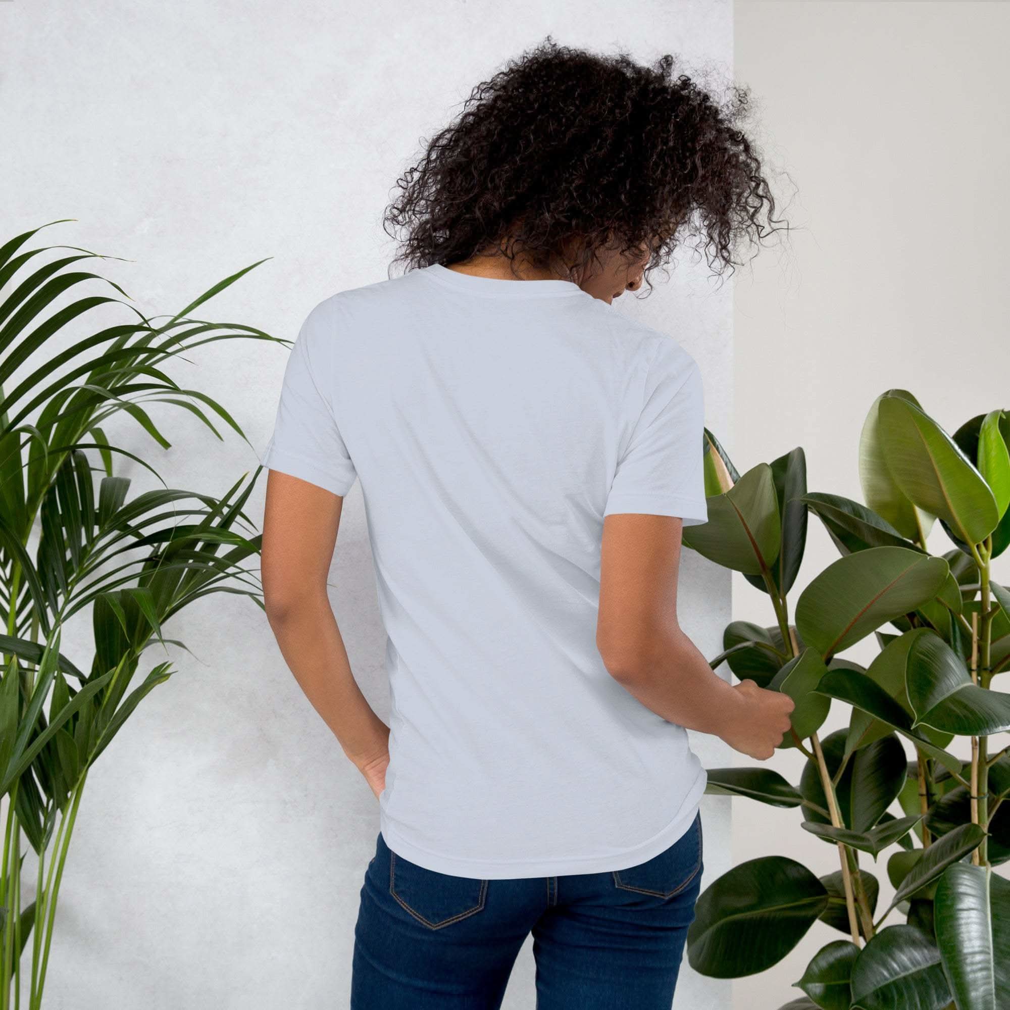 Woman wearing a plain white coffee t-shirt standing among green plants viewed from the back