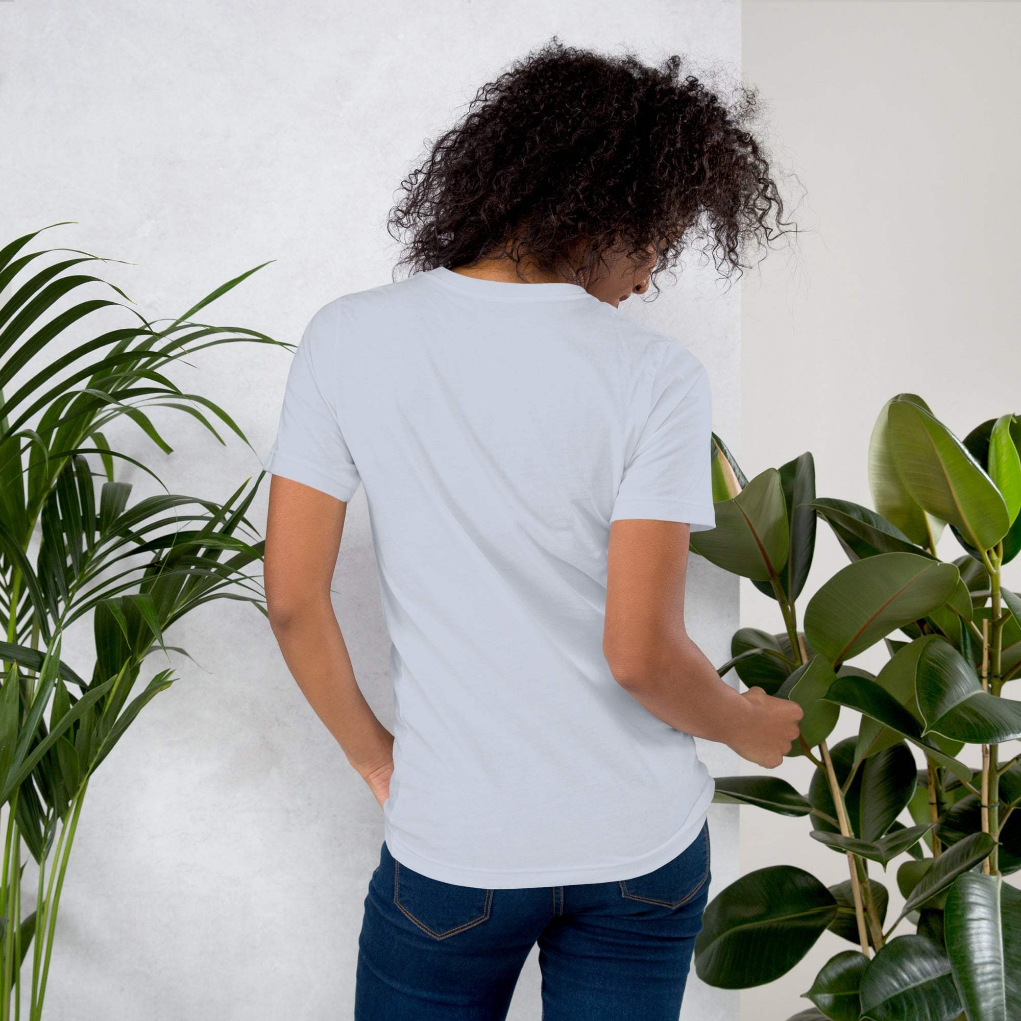 Woman wearing a plain white coffee t-shirt standing among green plants viewed from the back