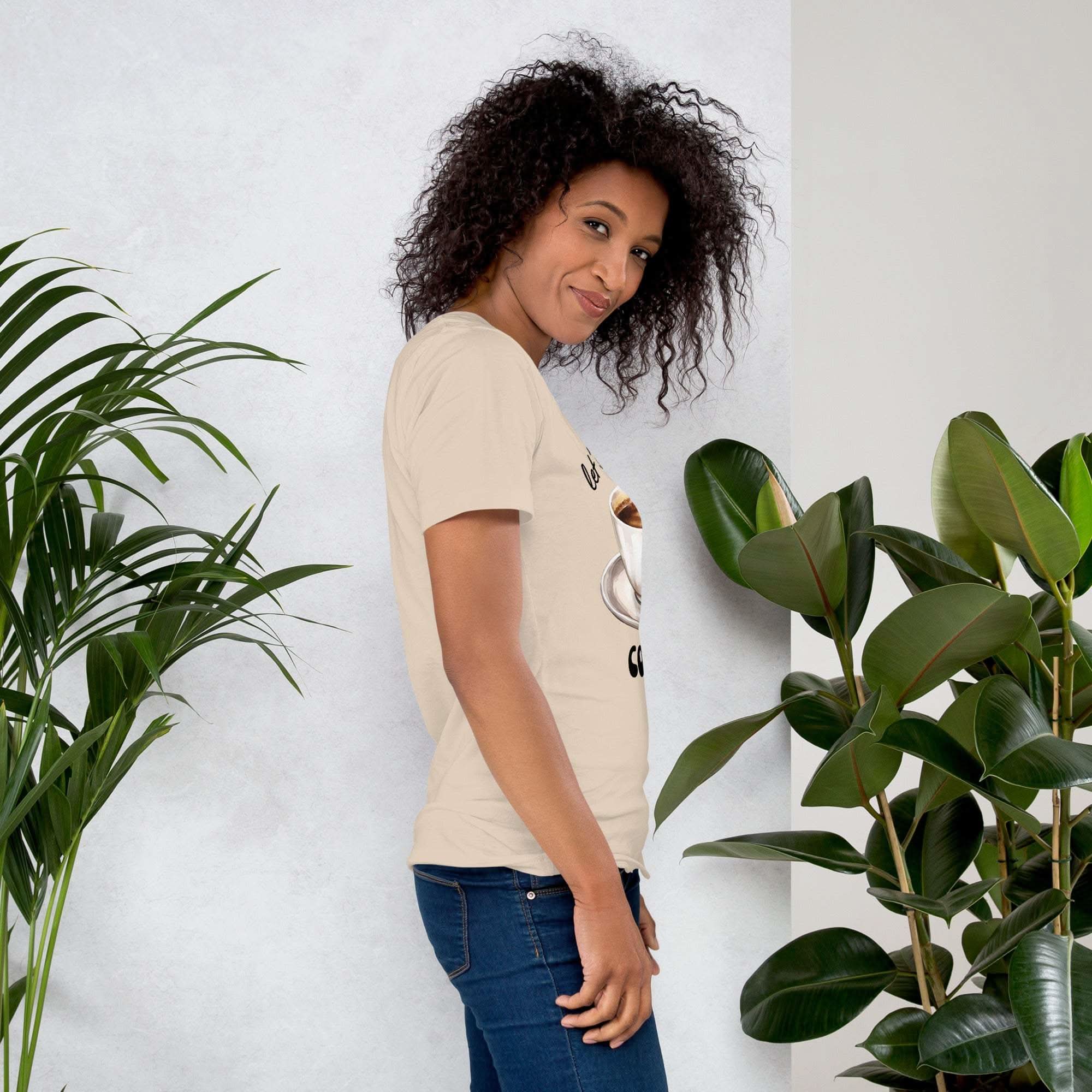 Woman wearing beige coffee t-shirt with coffee cup design standing near green plants