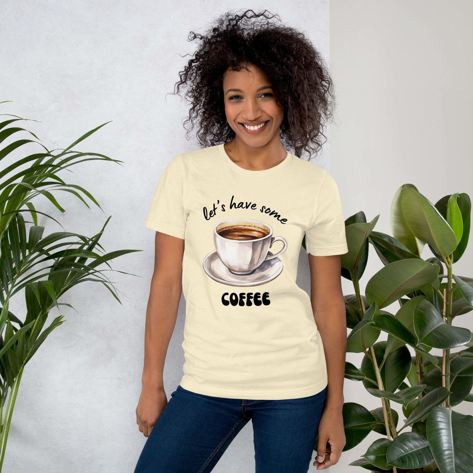 Woman wearing cream coffee t-shirt with "let's have some coffee" text and coffee cup graphic
