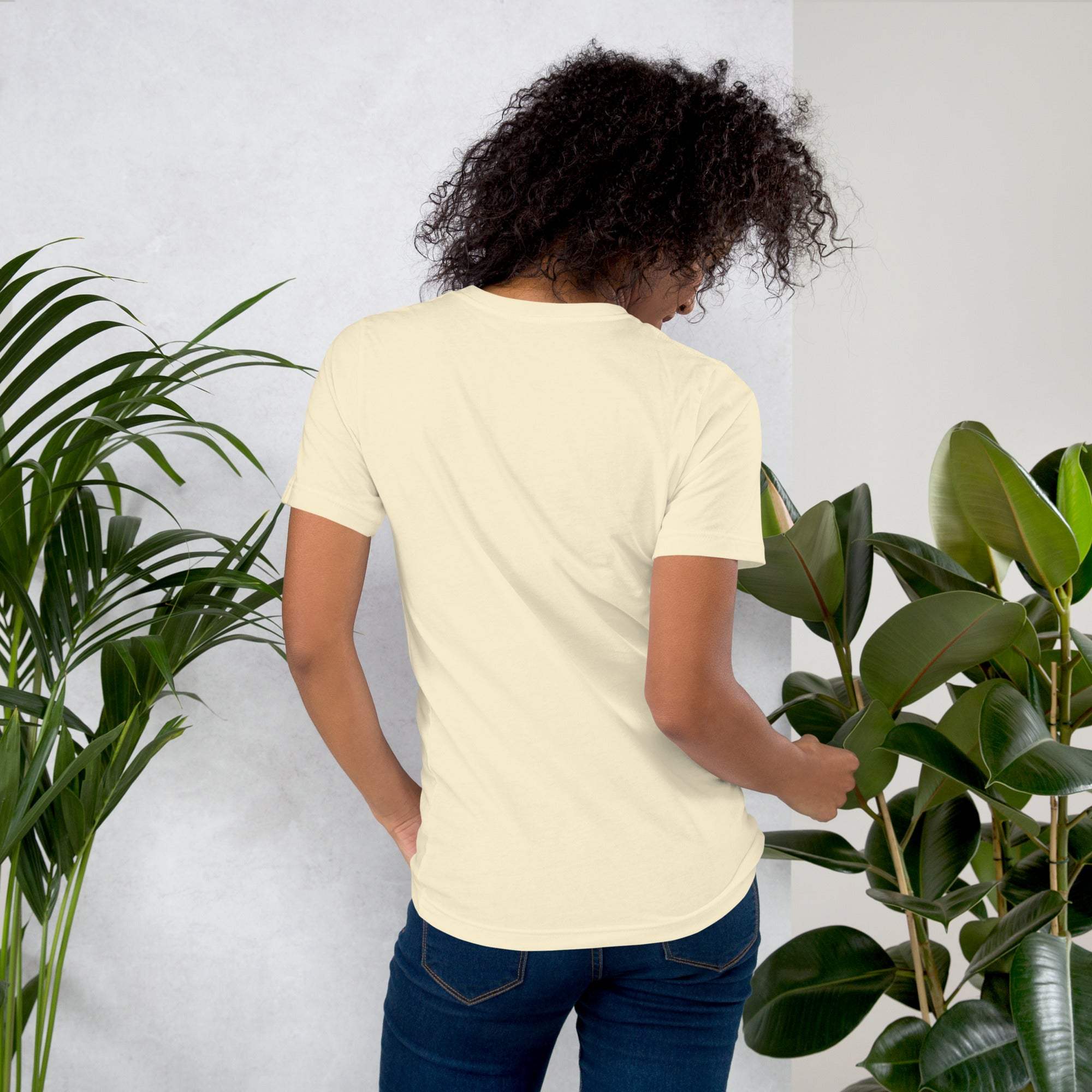 Woman wearing beige coffee t-shirt standing among green plants viewed from back