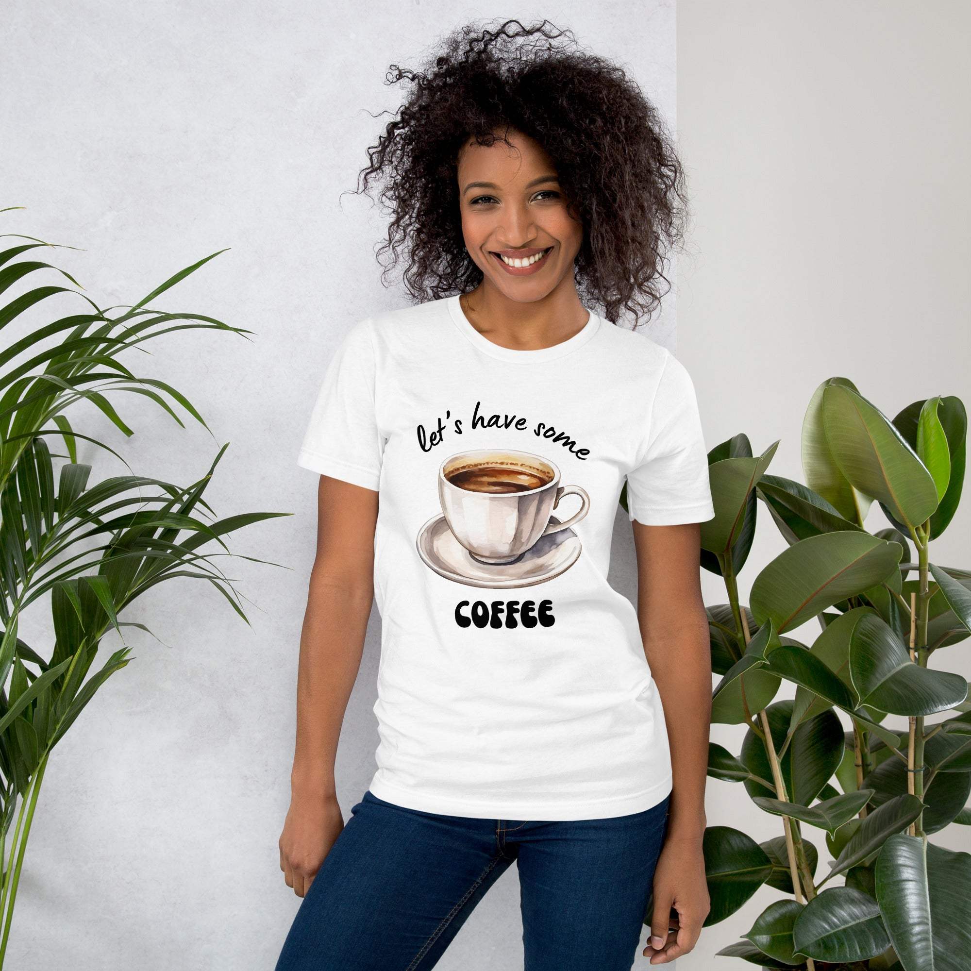 Woman wearing white coffee t-shirt with "Let's Have Some Coffee" text and cup design, standing near plants
