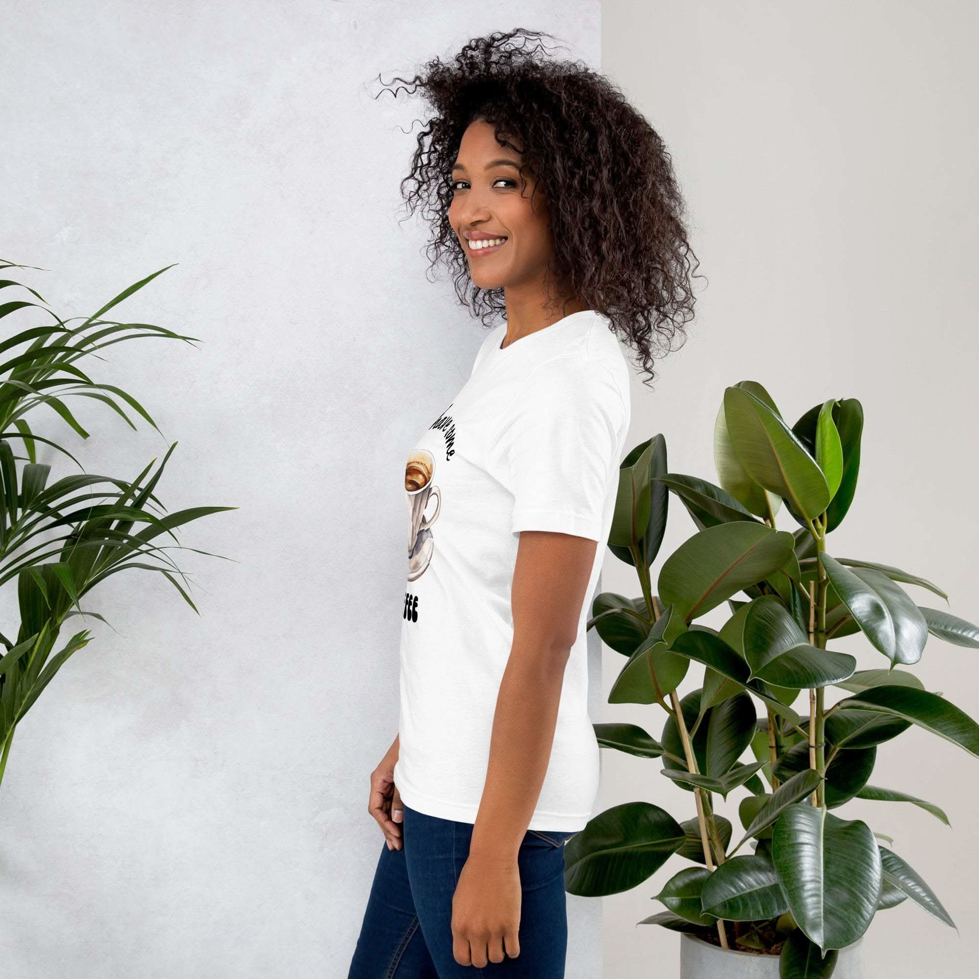 Woman wearing white "Let's Have Some Coffee" coffee-themed t-shirt standing by green plants