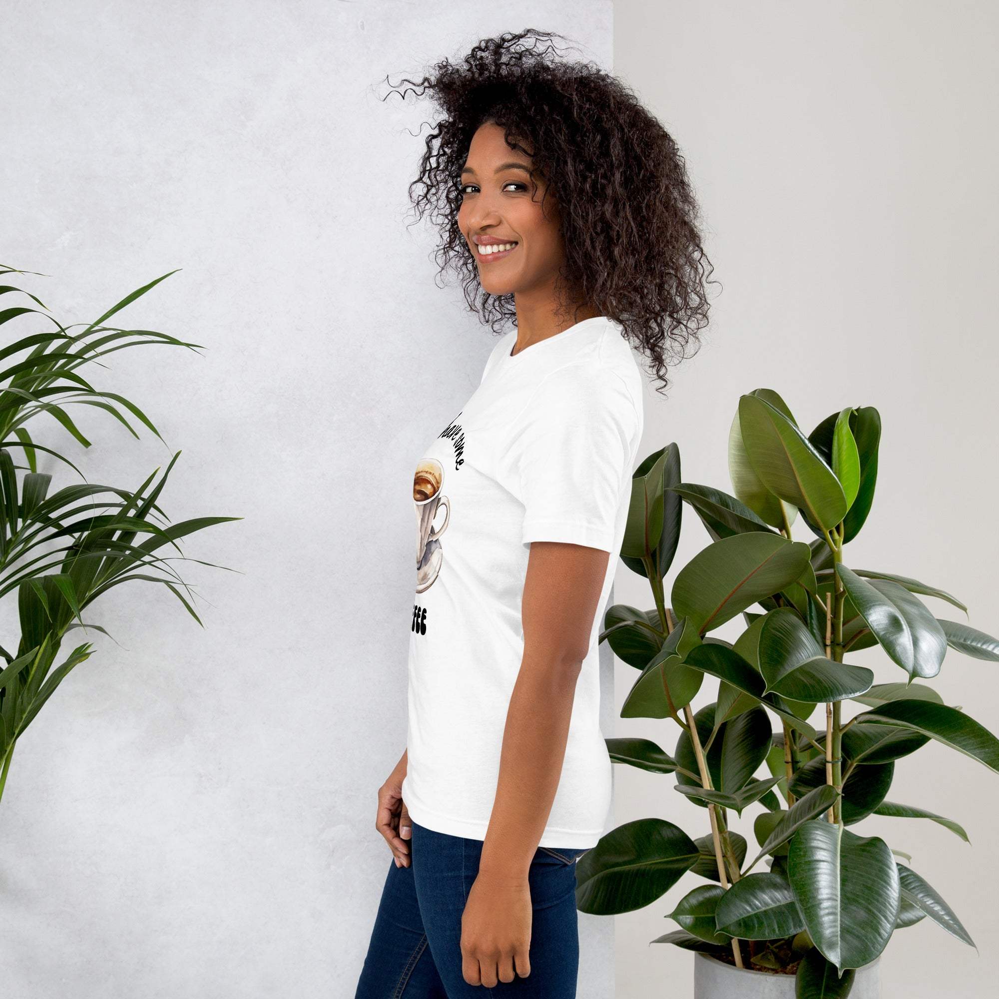 Woman wearing white "Let's Have Some Coffee" coffee-themed t-shirt standing by green plants