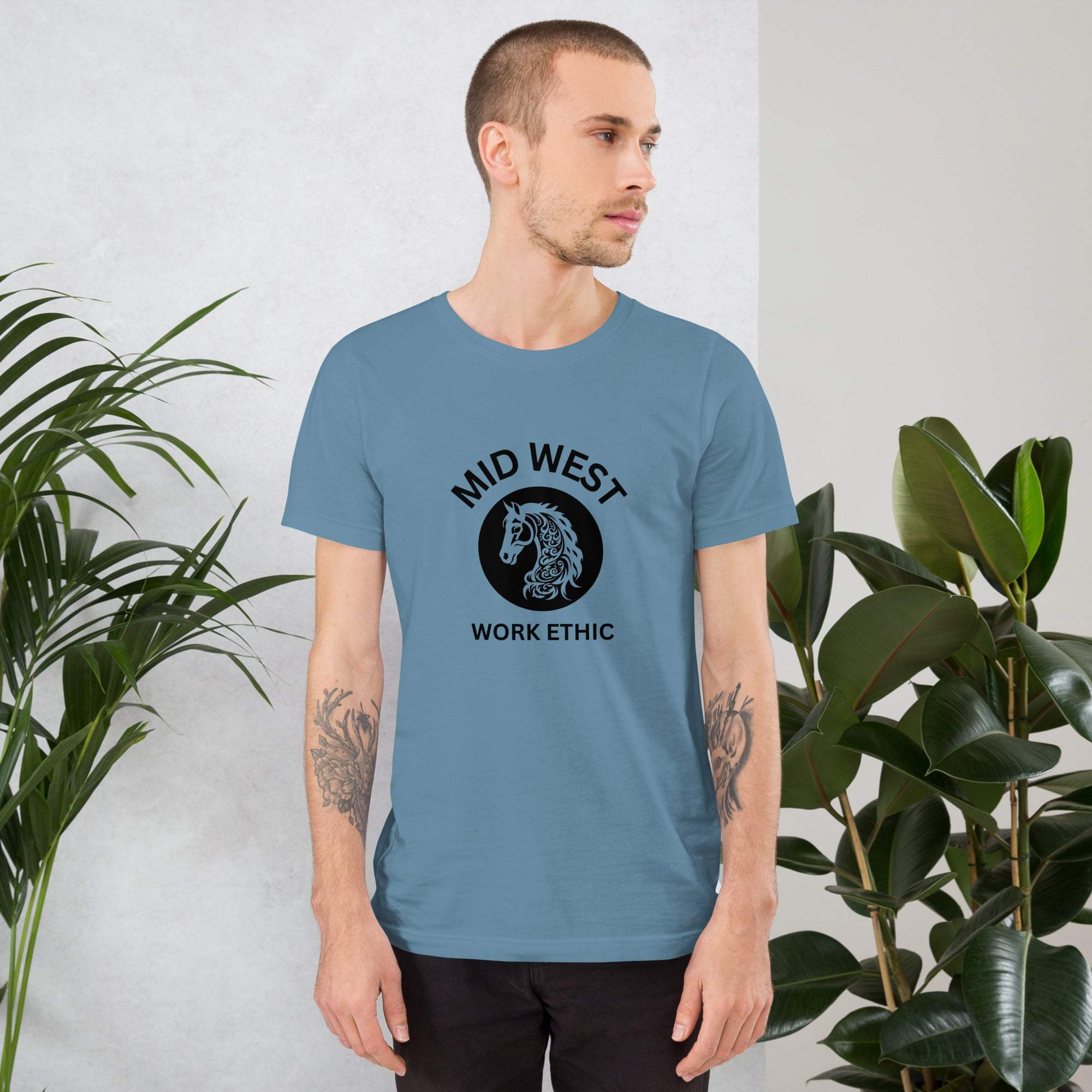 Man wearing blue Midwest T-Shirt with horse graphic and work ethic text standing near plants