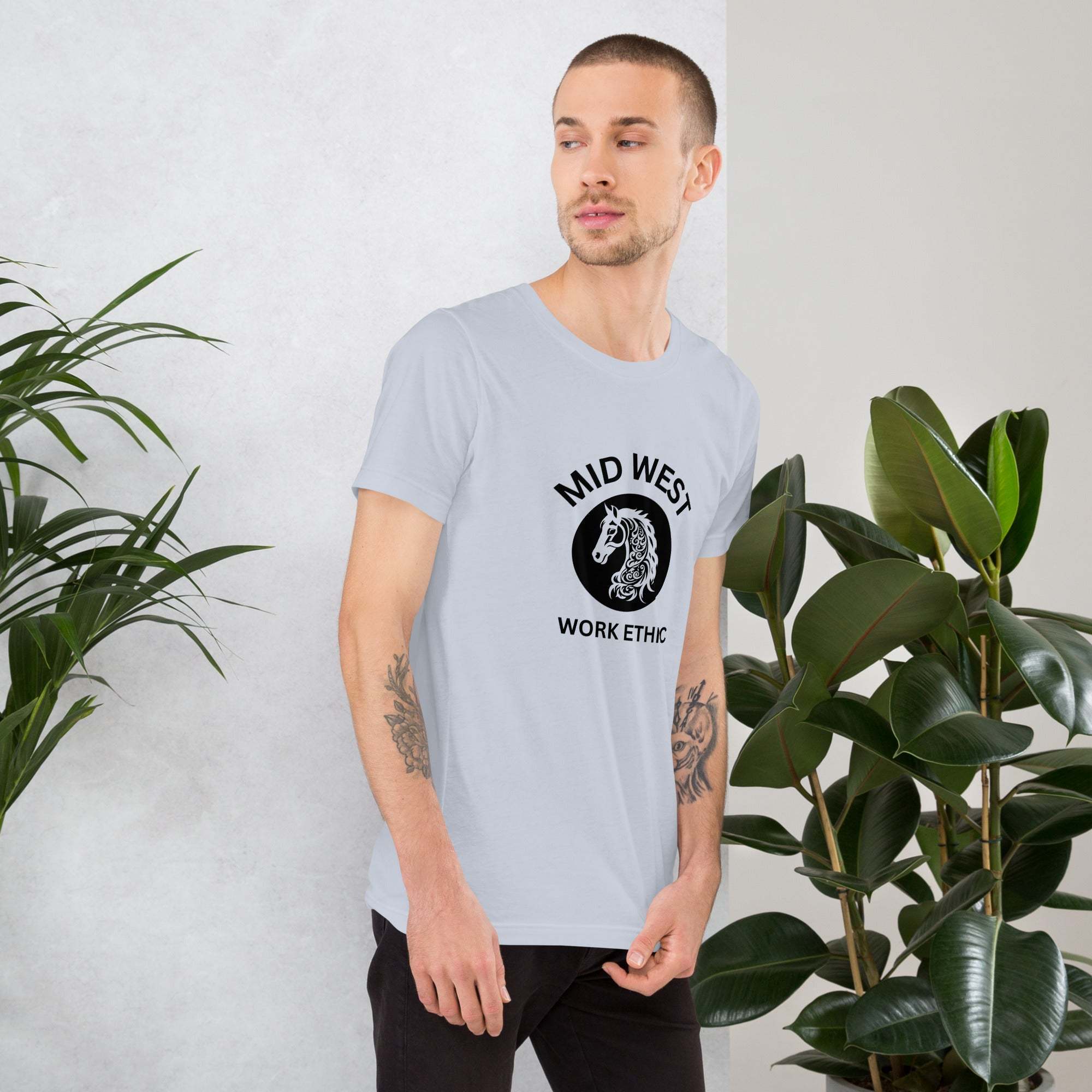 Man wearing light gray Midwest T-Shirt with black horse graphic and "Mid West Work Ethic" text standing near plants